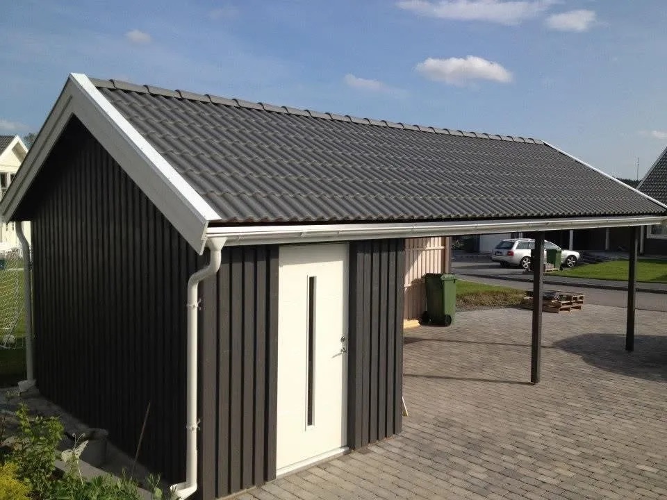 Nybyggt fristående garage med svart träfasad, sadeltak och ansluten carport i Stockholm.