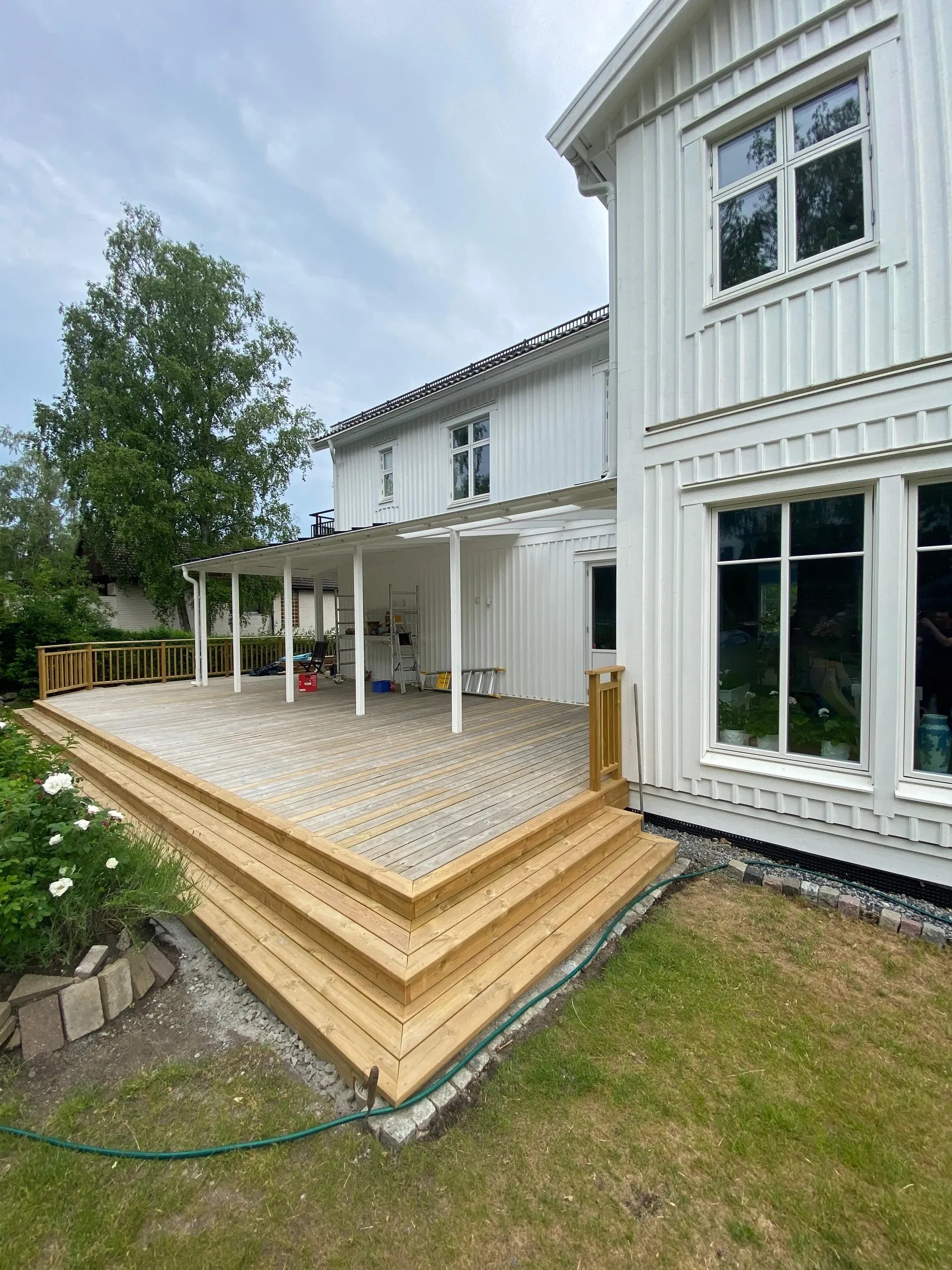 Tillbyggnad med en stor träaltan, trappa och tak intill en vit villa i Stockholm.