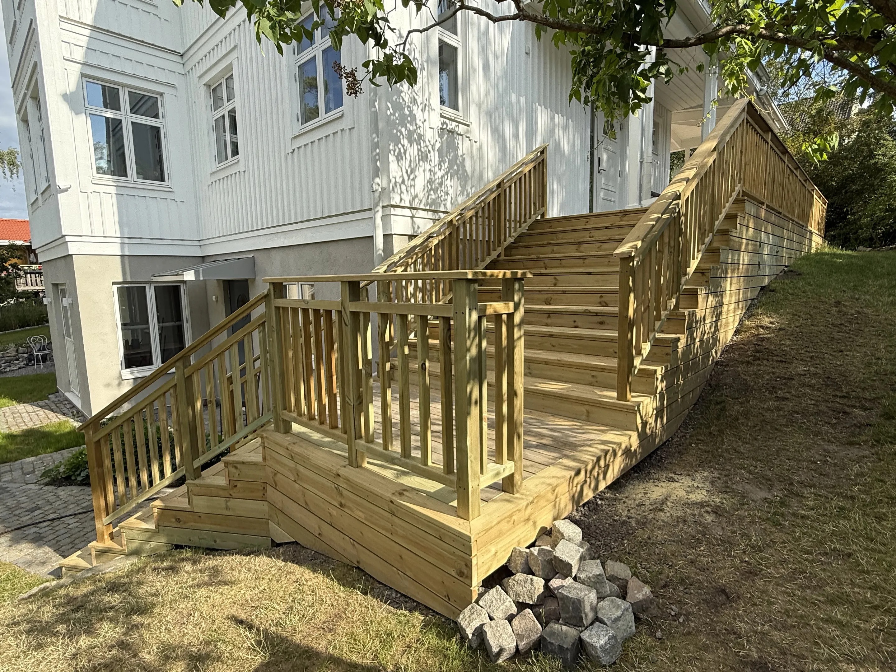 Tillbyggnad med en stor träaltan, trappa och tak intill en vit villa i Stockholm.