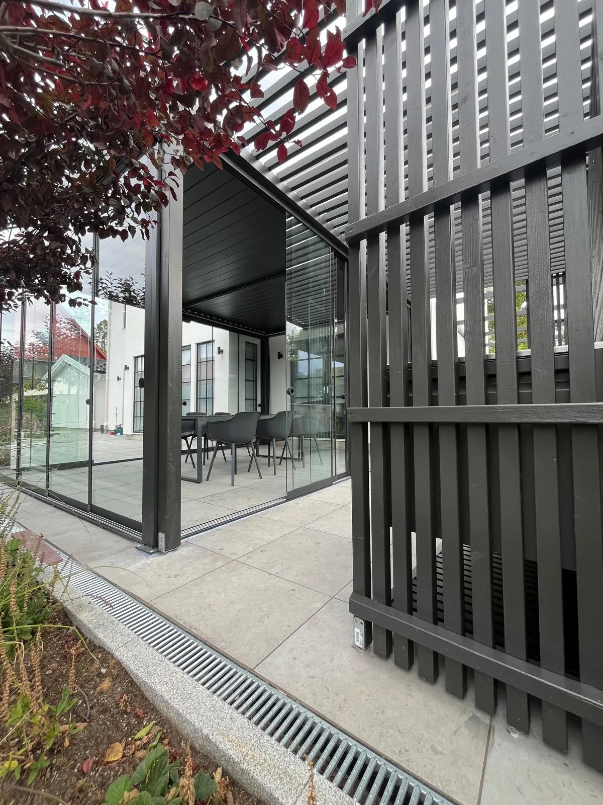 Platsbyggd svartmålad träpergola med ribbat insynsskydd intill en inglasad PERGOLUX pergola i Stockholm.