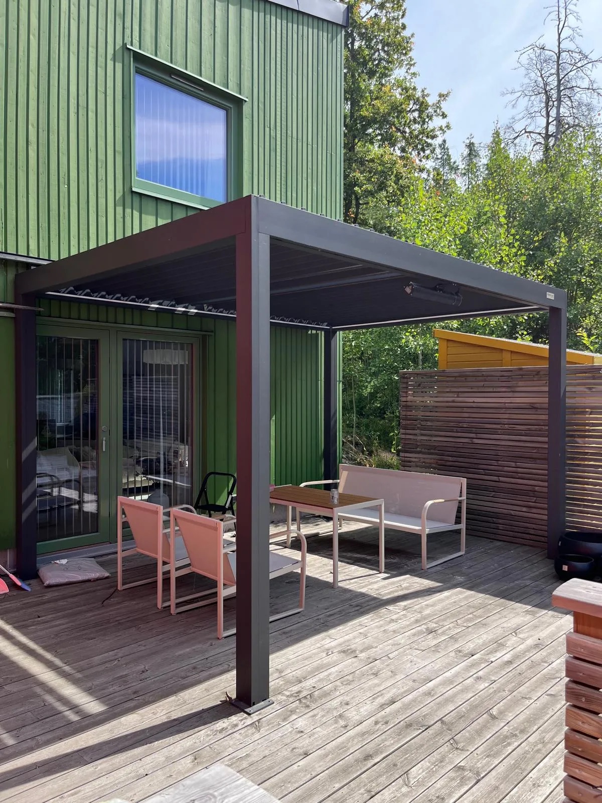 Mörkgrå PERGOLUX pergola monterad på träaltan vid grön villa